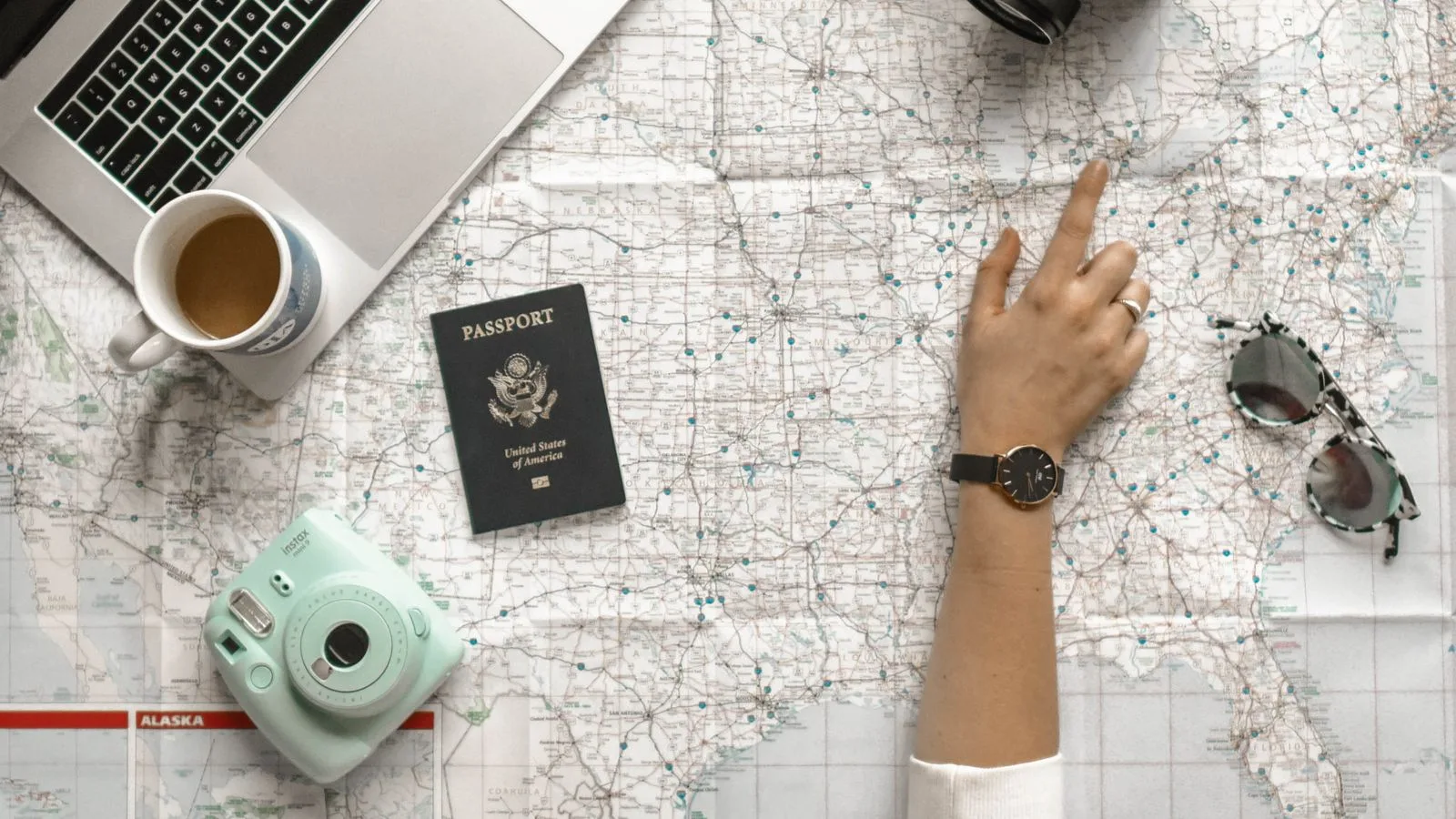Flat lay of a paper map, passport, camera and laptop used for planning a trip