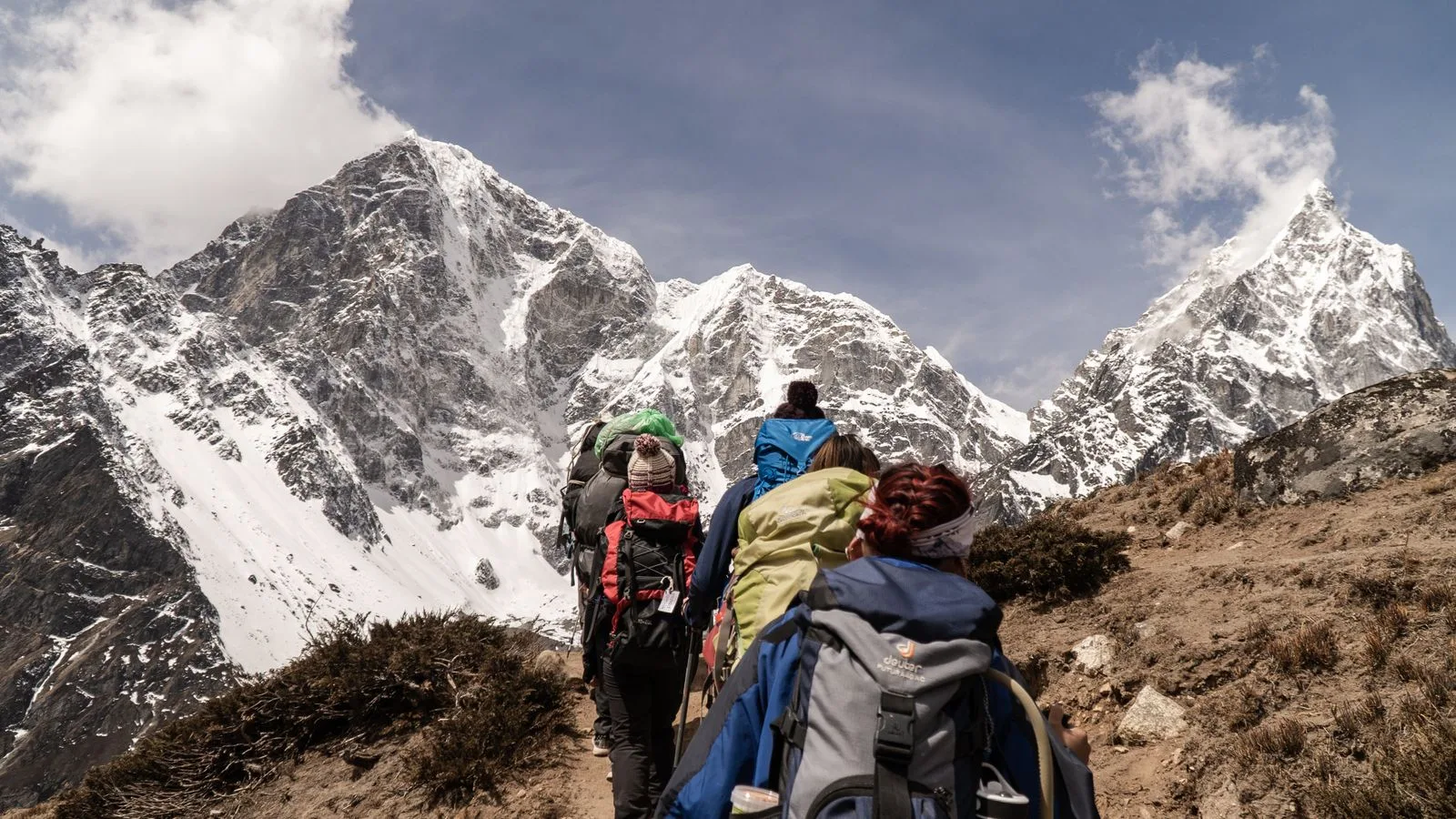 Trekking group with backpacks ascending a Himalayan trail toward snow-covered peaks in Nepal